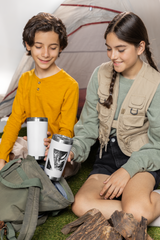 two young girls sitting on the ground next to a tent